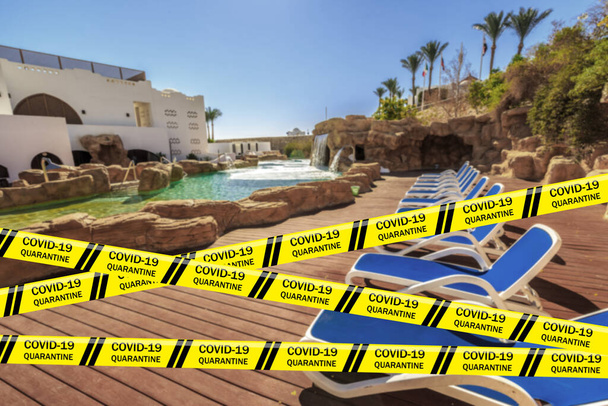 Biohazard Coronavirus warning tapes against swimming pool with artificial waterfall and sun loungers, luxury hotel, palm trees. Resort in Egypt. Quarantine. Pandemic COVID-19. Infectious disease - Photo, Image