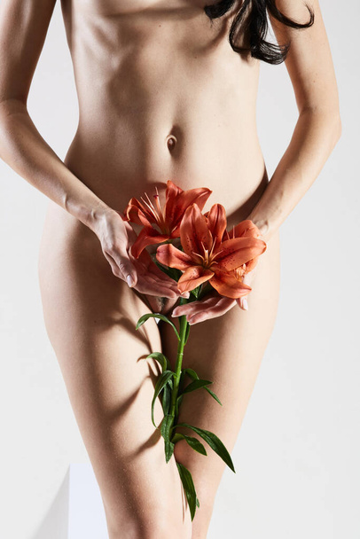 Intimate part of a womans body with flower in hands. Close up of a woman body with flower on her pubes. No retouch. - Foto, Imagen