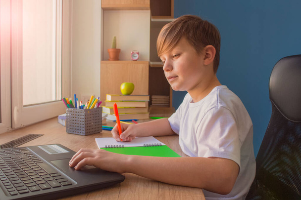 Menino feliz digitando em seu laptop, fazendo lição de casa, estudando on-line em casa na mesa de madeira perto da janela. Conceito de E-learning
 - Foto, Imagem
