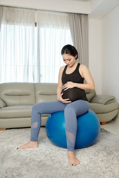 Pregnant young Vietnamese woman doing relaxing exercise on fitness ball at home - Photo, Image