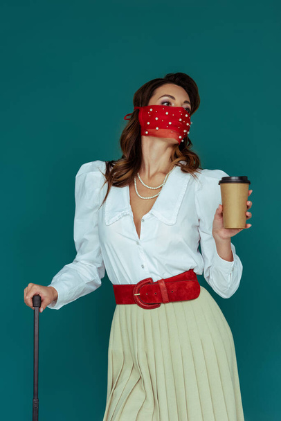 стильная девушка в красной маске, держащая кофе, чтобы уйти в изоляцию на синем
  - Фото, изображение