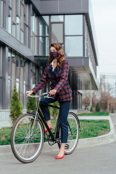 businesswoman w kratę maska jazda na rowerze w pobliżu budynku  - Zdjęcie, obraz