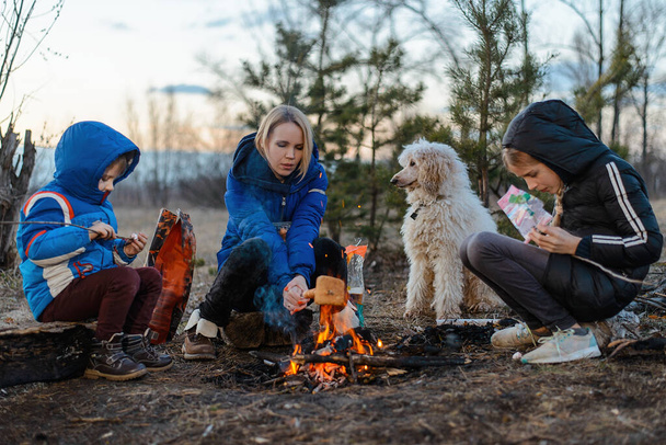 Madre, figlia e figlio sono seduti intorno al fuoco durante un picnic. Famiglia ricreazione all'aperto. Viaggiare, camminare, fermare il concetto
. - Foto, immagini