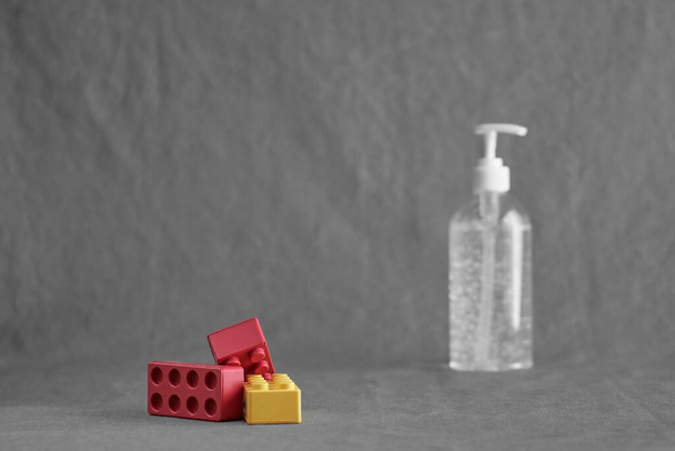 Una botella de plástico transparente blanco con gel desinfectante para manos con juguetes rojos y amarillos sobre un fondo gris. Concepto para coronavirus covid-19, educación e higiene en el hogar en la escuela, confinamiento y cuarentena
. - Foto, Imagen