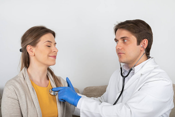 Young male doctor consulting female patient with influenza symptoms at home - Photo, Image