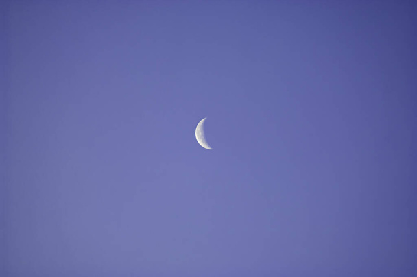 Berrak ve bulutsuz mavi gökyüzüne kurulmuş ince bir gümüş ay parçası.. - Fotoğraf, Görsel