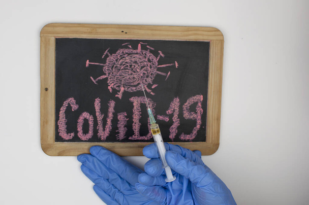 woman hands in blue medical glove hold Covid-19 word written on a small blackboard. Protection concept - Foto, Imagem