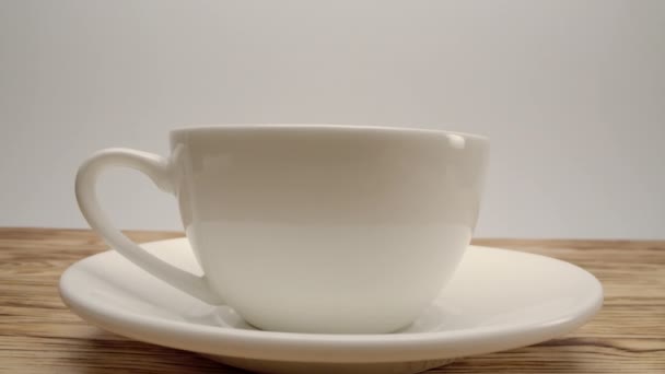 Λευκό φλιτζάνι καφέ σε ξύλινο τραπέζι και λευκό φόντο - Πλάνα, βίντεο