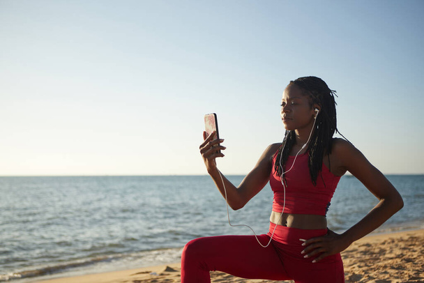 Pretty fit Black sportswoman taking selfie after working out of the beach - Photo, Image