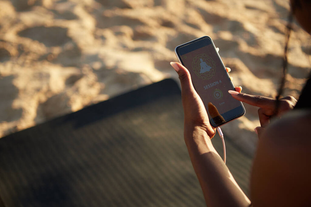 Imagen de cerca de la deportista de pie en la playa de arena y comenzar la sesión de yoga en el teléfono inteligente
 - Foto, Imagen
