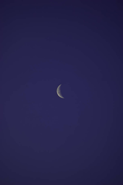 Egy vékony, ezüstös holddarab, mely a tiszta és felhőtlen kék ég kiterjedésén nyugszik.. - Fotó, kép