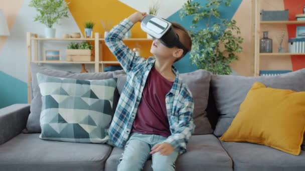 Joyful kid having fun with augmented reality glasses gesturing wearing headset at home - Materiał filmowy, wideo