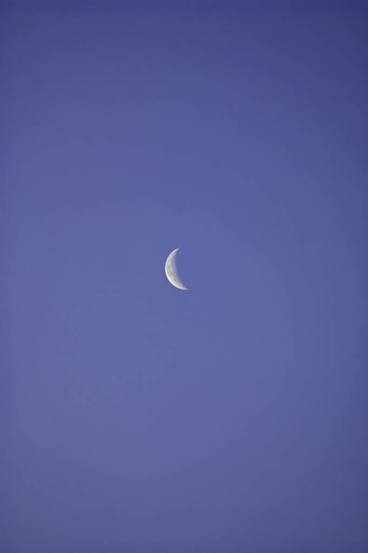 Una delgada astilla de luna plateada situada en una extensión de cielo azul claro y sin nubes
. - Foto, imagen