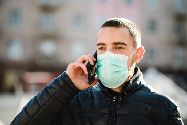 Coronavirus. Man wearing medical protective mask and talking on cell mobile phone, walking on street. Prevent Covid-19, flu. Virus, pandemic, panic concept. - Foto, afbeelding
