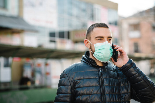 Coronavirus. Man wearing medical protective mask and talking on cell mobile phone, walking on street. Prevent Covid-19, flu. Feeling bad in city. Person needs help. Virus, pandemic, panic concept. - Фото, изображение