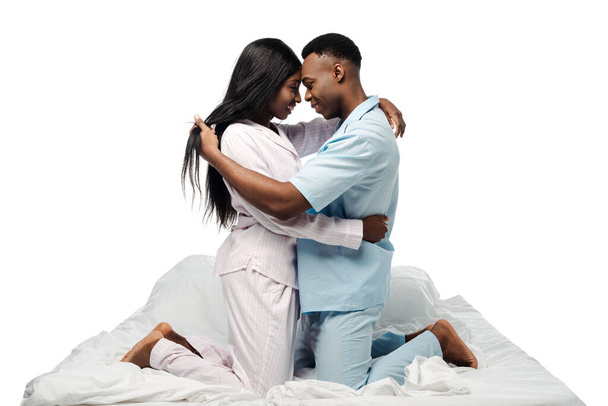 vista lateral de la feliz pareja afroamericana abrazándose en la cama en pijama aislado en blanco
 - Foto, imagen