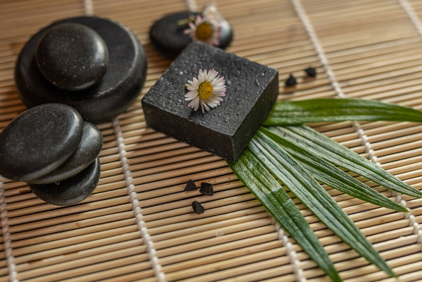 bar blok černého uhlí uhlí mýdlo na bambusovém pozadí s lávovými kameny lázeňský koncept - Fotografie, Obrázek