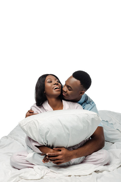 happy african american couple hugging pillow in bed in pajamas isolated on white - Valokuva, kuva