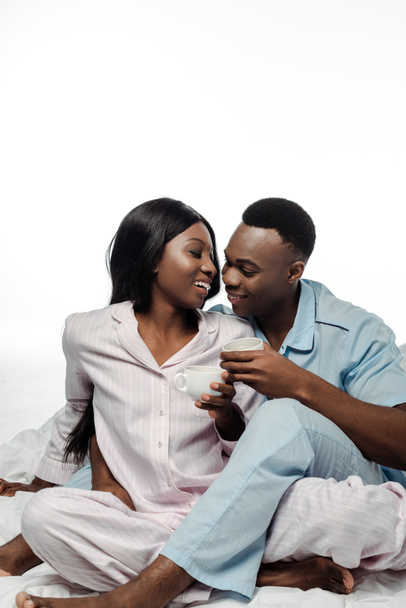 happy african american couple drinking coffee in bed in pajamas isolated on white - Photo, image