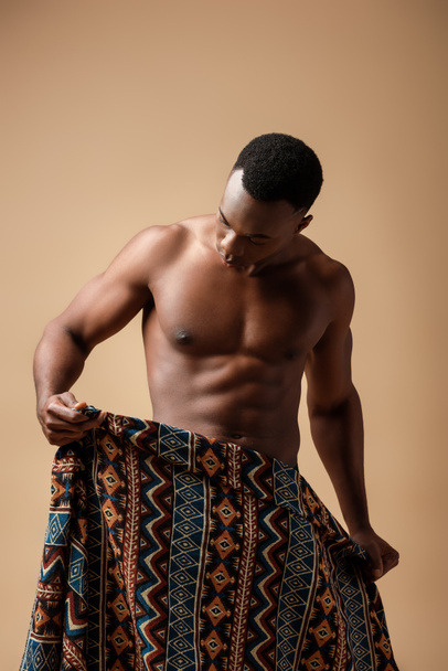 сексуальный голый племенной афро человек, покрытый одеялом, позирующий изолированно на бежевом
 - Фото, изображение