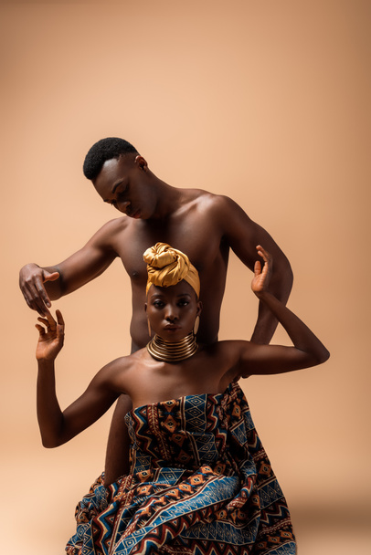 Battaniyeye sarılı seksi çıplak afro kadın bej giyen adamın yanında poz veriyor. - Fotoğraf, Görsel