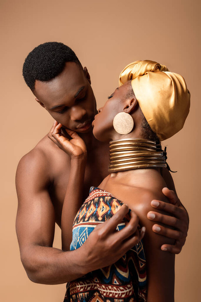 sexy naked tribal afro woman covered in blanket kissing man isolated on beige - Photo, Image
