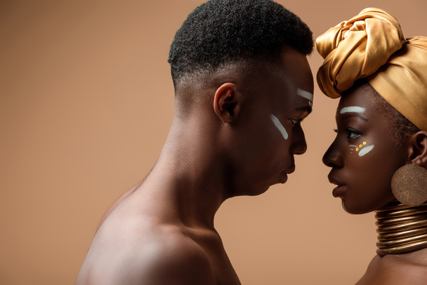vista lateral de la pareja afro tribal desnuda posando cara a cara en beige
 - Foto, Imagen