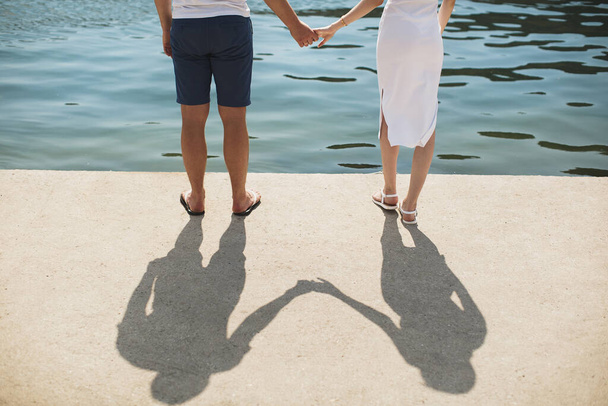Young couple boy and girl white dress holding hands on the background of water. - Photo, Image