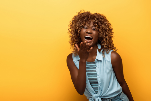 gelukkig afrikaanse amerikaanse vrouw lachen op gele achtergrond - Foto, afbeelding