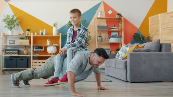 Sporty father doing push-ups with son on his back then falling feeling exhausted - Filmagem, Vídeo