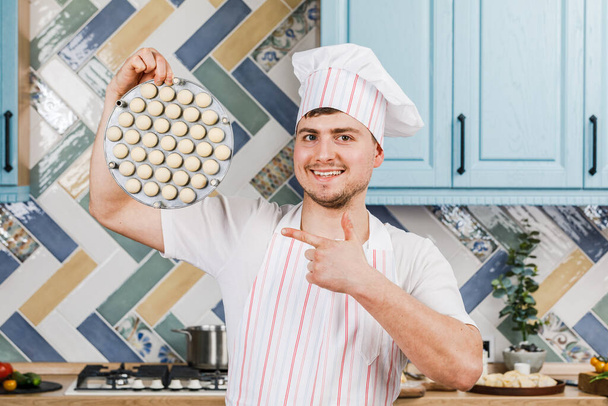 The cook in the kitchen holds dumplings in his hands and points at them with his hand . The concept of cooking - Фото, изображение