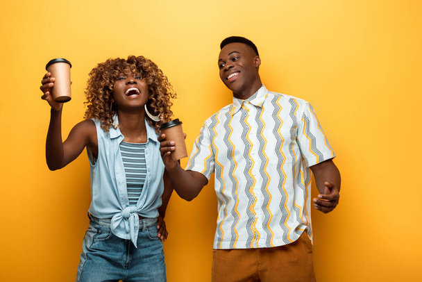 happy african american couple with paper cups on yellow colorful background - Fotoğraf, Görsel