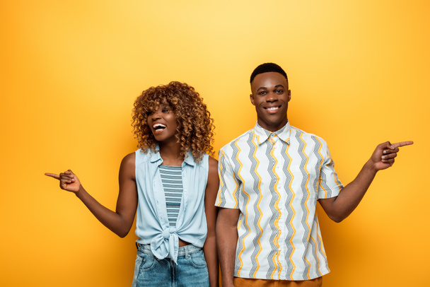 happy african american couple pointing with fingers on yellow colorful background - Foto, Imagem