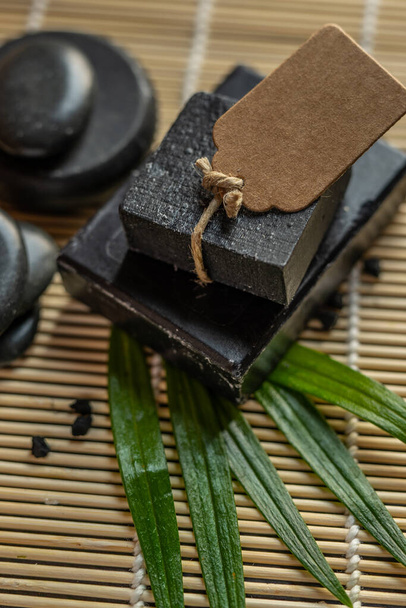 faszén szén fekete szappan bár egy nyers fa bambusz háttér láva kő spa bőrápolás higiéniai koncepció. Fekete fekete fekete kő backgroun. nyers fa háttér láva kő spa bőrápolás higiéniai koncepció - Fotó, kép