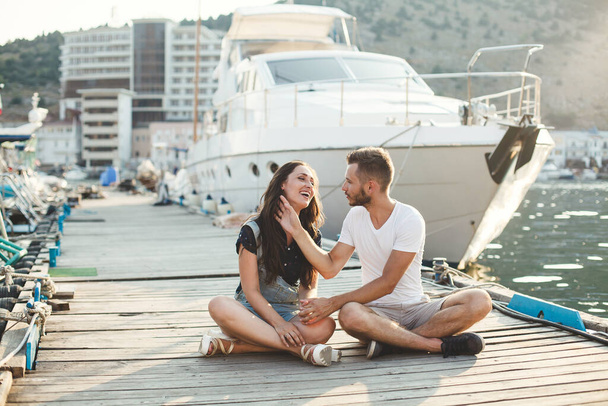 Lovers, guy and girl, are sitting on a wooden pier, holding hands and laughing - Foto, immagini