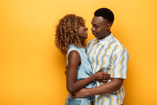 side view of happy african american couple hugging on yellow colorful background - Foto, Bild