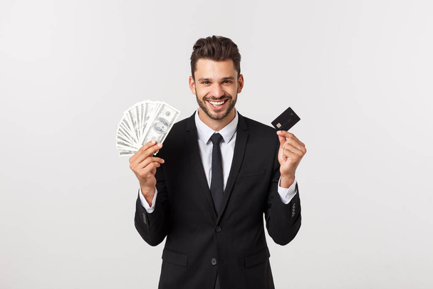 Νεαρός επιτυχημένος πλούσιος επιχειρηματίας με μαύρο κοστούμι που κρατά τραπεζογραμμάτια και πιστωτικές κάρτες που απομονώνονται σε λευκό φόντο για διαφήμιση. - Φωτογραφία, εικόνα