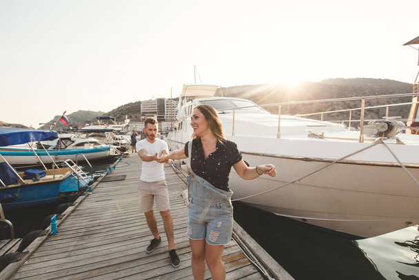 Lovers, boy and girl, walk and dance on the pier on the background of yachts and boats - Фото, зображення