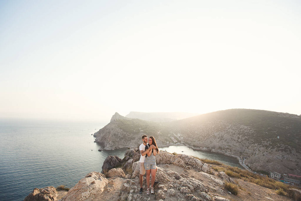 Lovers, guy and girl, on the edge of the cliff against the backdrop of mountains and ocean - Fotografie, Obrázek