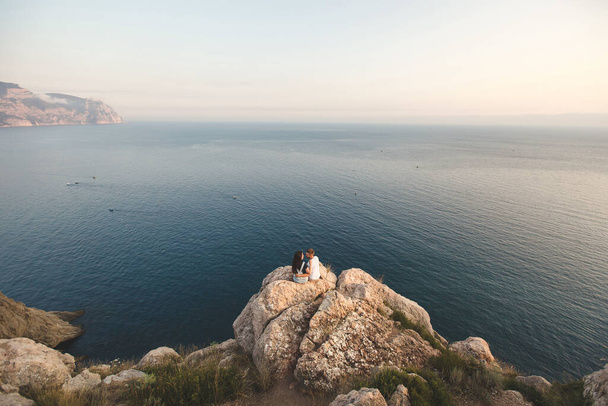 Lovers, guy and girl, on the edge of the cliff against the backdrop of mountains and ocean - Foto, Imagem