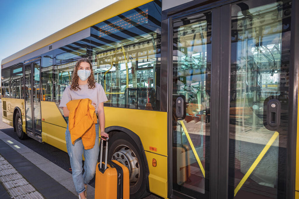 Retrato de uma adolescente na estação de ônibus com uma máscara facial médica como medida contra a infecção viral ou bacteriana
 - Foto, Imagem