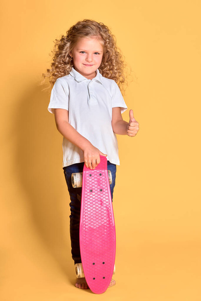 Active and happy girl with curly hair, headphones having fun with penny board, smiling face stand skateboard. Penny board cute skateboard for girls. Lets ride. Girl ride penny board yellow background. - Photo, Image