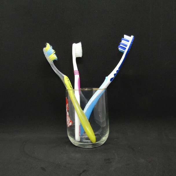 Tandenborstels van verschillende kleuren in een glazen Beker. - Foto, afbeelding