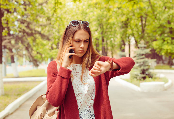 Late. Woman angry looking at wristwatch talking at phone with boyfriend  who is late for the date isolated outdoors park background - 写真・画像