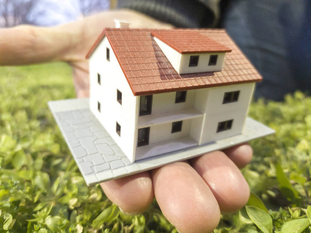 Инвестиции в недвижимость. Новая концепция строительства домов. Мужские руки и пальцы, держащие модель дома
 - Фото, изображение