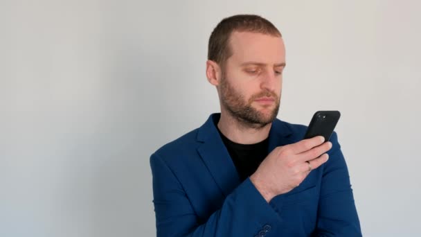 young handsome businessman with blue eyes in a blue jacket looking at the camera and reads a message on the phone - Πλάνα, βίντεο