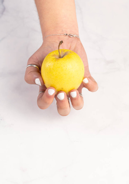 Yellow apple in hands on a marble background - Foto, immagini