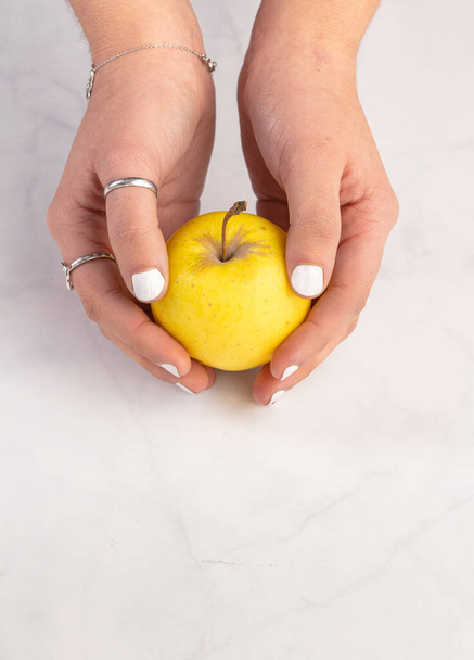 Yellow apple in hands on a marble background - Valokuva, kuva