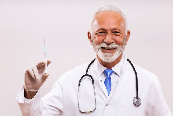 Portrait of senior doctor holding injection on gray background. - Фото, изображение
