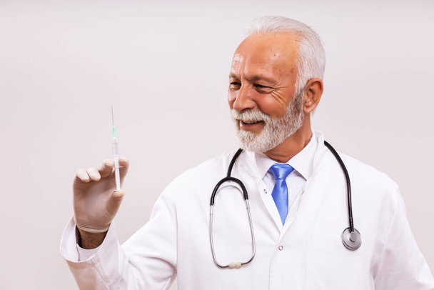 Portrait of senior doctor holding injection on gray background. - Foto, Bild